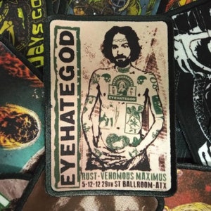 May include: A white patch with a black border featuring a black and white image of a tattooed man with the text "EYEHATEGOD" in green and white. The text "RUST-VENOMOUS MAXIMUS 5-12-12 29TH ST BALLROOM-ATX" is printed in black at the bottom.