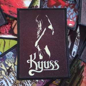 May include: A dark purple patch with a white silhouette of a woman and the word "Kyuss" in white cursive lettering.