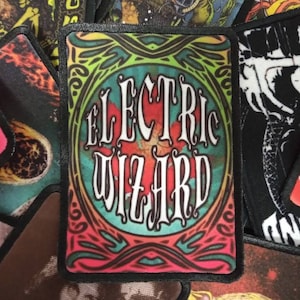 Peut inclure: Un patch brodé coloré avec le texte "EL ELECTRIC WIZARD" dans un design circulaire avec une bordure noire.