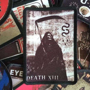 May include: A black and white embroidered patch with a skeletal figure in a hooded robe holding a scythe. The patch has the text "DEATH XIII" at the bottom.