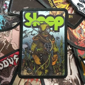 May include: A black and green embroidered patch with the word "Sleep" in green letters. The patch features a scuba diver in a yellow diving suit with a helmet. The background is a blue ocean with fish and seaweed.