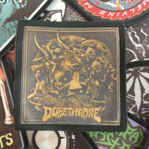May include: A black and gold embroidered patch featuring the band name "Dope Throne" and a graphic of a skull with horns and a third eye. The skull is surrounded by mushrooms and other imagery.