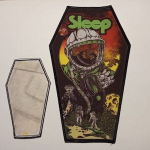Puede incluir: Un parche de hierro bordado en negro y verde que presenta un astronauta con un traje espacial verde sobre un fondo rojo y amarillo. El texto "Sleep" está en letras verdes en el parche.