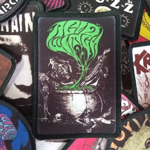 May include: Black and green embroidered patch featuring a cauldron with a green plant growing out of it. The text "Seed Witch" is above the cauldron.