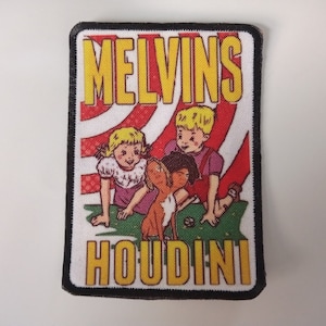 Può includere: Una toppa bianca e nera con uno sfondo a strisce rosso, bianco e blu. La toppa presenta uno stendardo giallo con il testo "MELVINS HOUDINI" e un'illustrazione di tre bambini e un cane.