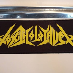 Puede incluir: Parche bordado amarillo con la palabra "Toxic Holocaust" en una fuente estilizada sobre un fondo negro.