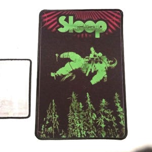 May include: A black and green patch with the word "Sleep" in green letters. The patch features a green astronaut floating in space with green plants in the background.