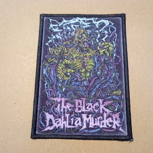 May include: Black and white embroidered patch featuring a graphic of a monstrous creature with a purple and green design. The text "The Black Dahlia Murder" is printed in pink.