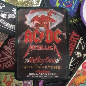 May include: A black and white patch with the text "AC/DC", "METALLICA", "Motley Crue", "QUEENSRYCHE", "Donington Park", "Saturday 17th August 1991". The patch features a red devil with wings in the background.