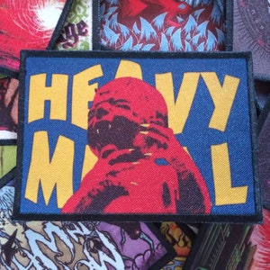 May include: A blue and yellow embroidered patch with the text "Heavy Metal" and a red and black illustration of a person's head.