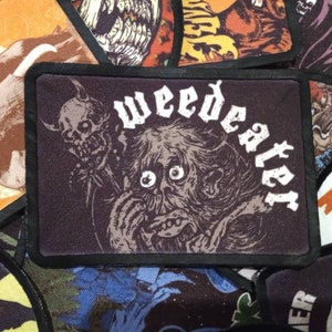 May include: Black and white embroidered patch with a monster with large eyes and the word "weed eater" in white lettering.