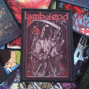 May include: A black and red embroidered patch with the band name "Lamb of God" in white lettering. The patch features a hooded figure holding a scythe in front of a red background.