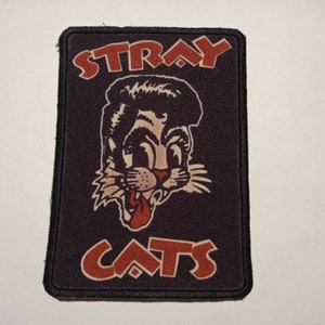 May include: A black and red embroidered patch with the words "Stray Cats" and a cartoon cat with a pompadour hairstyle.