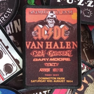Peut inclure: Un patch noir et orange avec le texte "Monsters of Rock" et les noms de groupes dont AC/DC, Van Halen, Ozzy Osbourne, Gary Moore et Accept. Le patch comprend également la date "Samedi 18 août 1984" et le lieu "Donington Park".