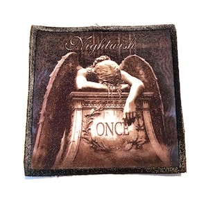 Op de afbeelding: Een bruin en zwart geborduurde patch met de bandnaam "Nightwish" en het woord "Once" in een krans. De patch toont een sepia-kleurige afbeelding van een engel met vleugels, die leunt op een stenen structuur.