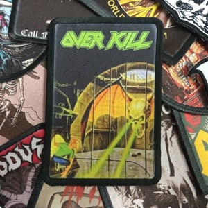 Op de afbeelding: Een zwart en groen geborduurd patch met de tekst "OVER KILL" in groene letters. De patch heeft een afbeelding van een demon met vleugels en een schedelgezicht, die groene lasers uit zijn ogen schiet.