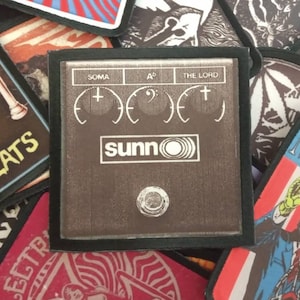 May include: A black and brown patch with the text "sunn" and "THE LORD" in white. The patch has three knobs labeled "SOMA", "A", and "THE LORD".