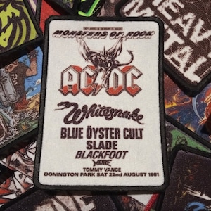 May include: A white patch with black trim featuring a Monsters of Rock concert poster. The poster features the band AC/DC in red and black with a lightning bolt. The poster also lists the bands Whitesnake, Blue Oyster Cult, Slade, Blackfoot, and Tommy Vance. The concert took place at Donington Park on August 22, 1981.