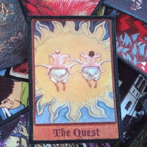 May include: A vintage-style tarot card featuring a yellow sun and two figures riding winged creatures. The card is titled "The Quest".