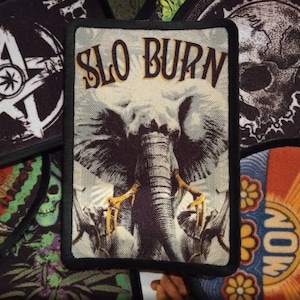 May include: A black and white embroidered patch featuring a brown elephant and the text "SLO BURN" in yellow lettering.