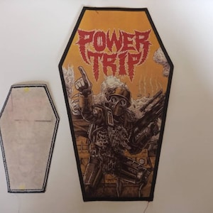 May include: A black and yellow coffin-shaped patch with a red and white "POWER TRIP" logo and a drawing of a soldier wearing a gas mask and holding a gun.