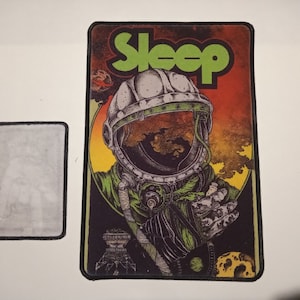 May include: A black and white patch with a green and yellow illustration of an astronaut wearing a helmet. The text "Sleep" is in green letters at the top of the patch.