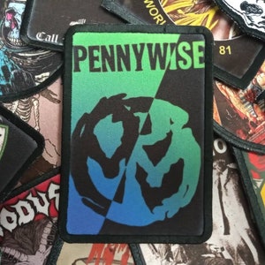 May include: A black and green embroidered patch with the band name "PENNYWISE" in white text and a blue and green swirl design. The patch has a black border and the number "81" in white text in the top right corner.