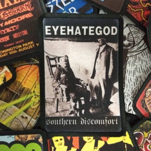 May include: A black and white band patch with the text "EYEHATEGOD" and "southern discomfort" in white. The patch features a black and white photo of two people.