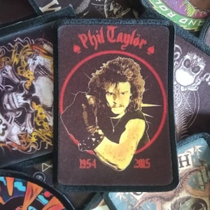 May include: A black and white embroidered patch with a skull and flames. The patch has the text "1983" on it.