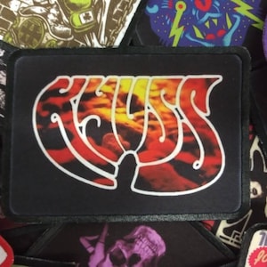 May include: Black and red embroidered patch with the word "KISS" in a stylized font. The patch has a black background and a red and orange design.