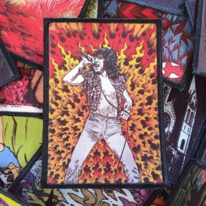 Könnte beinhalten: Ein gestickter Patch mit einem Schwarzweißbild einer Person, die in ein Mikrofon singt, vor einem feurigen orangefarbenen und gelben Hintergrund.