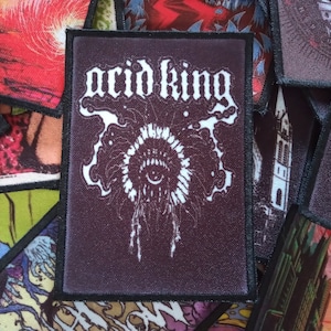 May include: A black and white embroidered patch with the text "acid king" in white lettering. The patch features a stylized eye with a white background and a black outline.