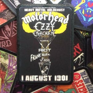 Peut inclure: Un patch noir et jaune avec le texte "Heavy Metal Holocaust" et "Motorhead" en grandes lettres blanches. Le patch présente également les noms d'autres groupes, dont "CZZY", "Ozbourne", "Triumph", "Riot", "Frank Marino", "Vardis" et "Port Vale". La date "1 août 1981" est imprimée en bas du patch.