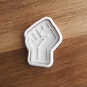 May include: White plastic cookie cutter shaped like a raised fist.