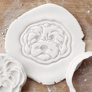 May include: White plastic cookie cutter shaped like a dog's head. The cookie cutter is on a white surface.