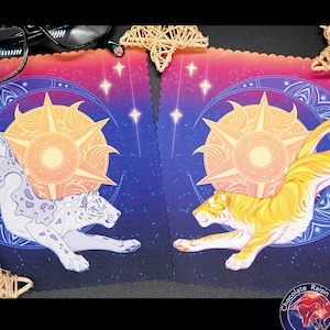 May include: Two playing cards with a blue and purple background. The cards feature a white and gray snow leopard and a yellow and orange tiger jumping in front of a sun and stars. The cards have a scalloped edge and the text "Chocolate Raisin Fury" is on the bottom right corner.