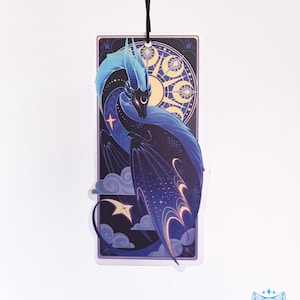May include: A blue and purple dragon with a starry pattern on its wings is depicted in a decorative frame. The dragon is surrounded by clouds and stars, and the frame features a sun and moon design.