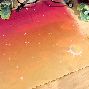 Puede incluir: Un pa&ntilde;o de microfibra rojo, naranja y amarillo con un dise&ntilde;o de luna creciente y estrellas blancas. El pa&ntilde;o tiene un borde festoneado.