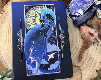 May include: A dark blue notebook with a celestial dragon design. The dragon is blue and purple with gold accents and is surrounded by stars and clouds. The notebook has a gold border and a gold title that reads "Celestial Dragon".