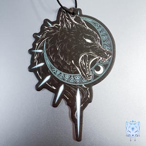 May include: Black and white car air freshener with a wolf howling at the moon. The wolf is surrounded by a circle of Celtic knots and the moon is crescent shaped. The air freshener is shaped like a teardrop with a string for hanging.