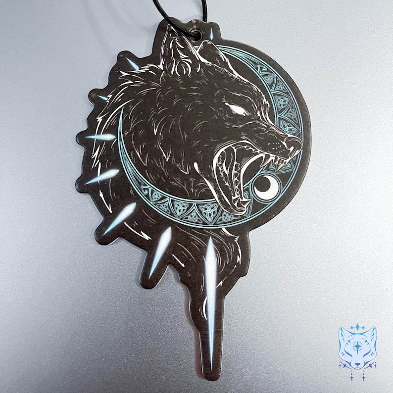 May include: Black and white car air freshener with a wolf howling at the moon. The wolf is surrounded by a circle of Celtic knots and the moon is crescent shaped. The air freshener is shaped like a teardrop with a string for hanging.