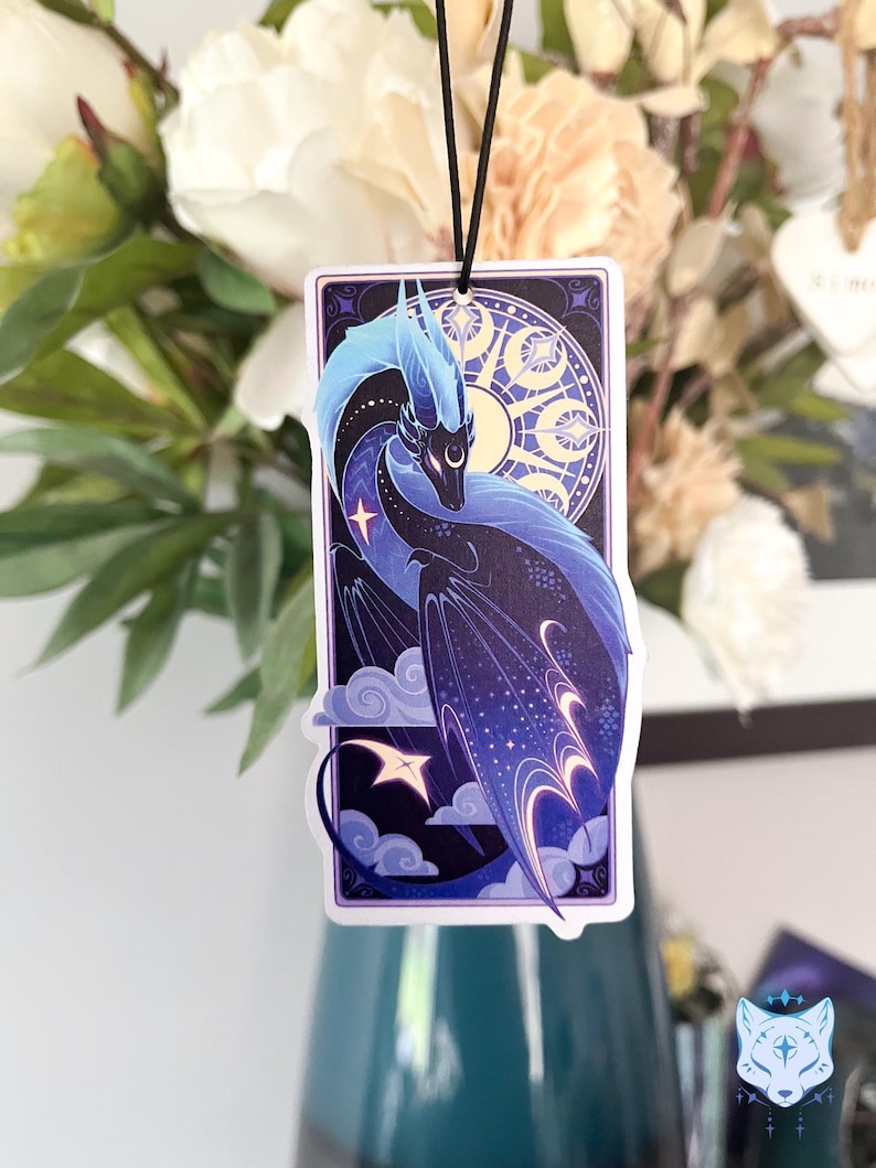Pu&ograve; includere: Un drago blu e viola con stelle e lune sulle ali, su uno sfondo blu scuro con nuvole. Il drago &egrave; in una cornice bianca con un bordo viola.