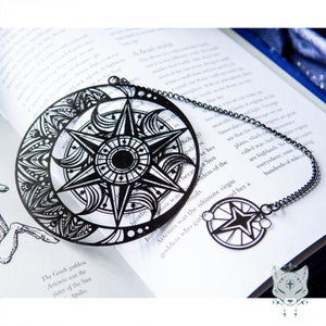 Puede incluir: Marcapáginas de metal negro con un diseño de sol y luna con intrincados detalles. El marcapáginas está unido a una cadena con un pequeño amuleto en forma de estrella.