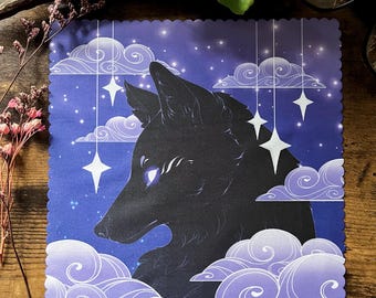 May include: A square print featuring a black wolf silhouette against a starry night sky. The design includes white clouds and hanging stars, with a scalloped edge. The color palette is primarily blue, purple, and white.