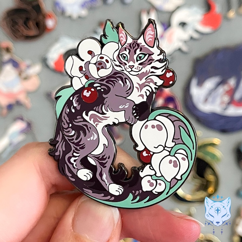 May include: A purple and white enamel pin featuring a cat curled around a bouquet of white flowers with red berries. The cat has a white face and a fluffy tail.