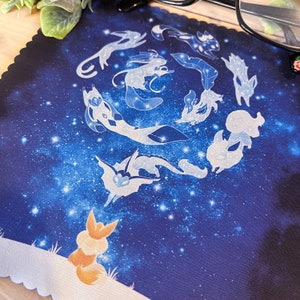 May include: A blue and white microfiber cleaning cloth with a galaxy print and a design of nine white foxes with stars in their tails. A single orange fox is looking up at the sky.
