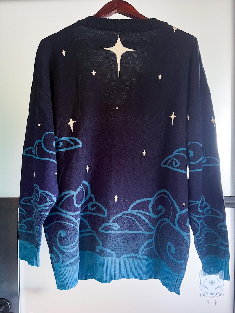 May include: Navy blue sweater with a celestial design. The sweater features a pattern of white stars and stylized blue clouds against a dark blue background. The cuffs and hem are a lighter shade of blue.