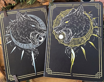 Pode incluir: Dois diários de couro preto com detalhes dourados. As capas apresentam um design de lobo preto e branco com um motivo de lua e sol. Um lobo está rodeado por uma lua branca e o outro por um sol amarelo.