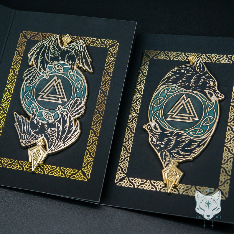May include: Two black and gold enamel pins with a green and blue background. The pins feature a raven and a wolf, both with a triangular symbol in the center.