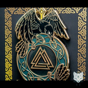 May include: A black and gold enamel pin featuring a raven perched on a circular design with a gold Valknut symbol. The raven has a green background and the Valknut is surrounded by a gold Celtic knot design.